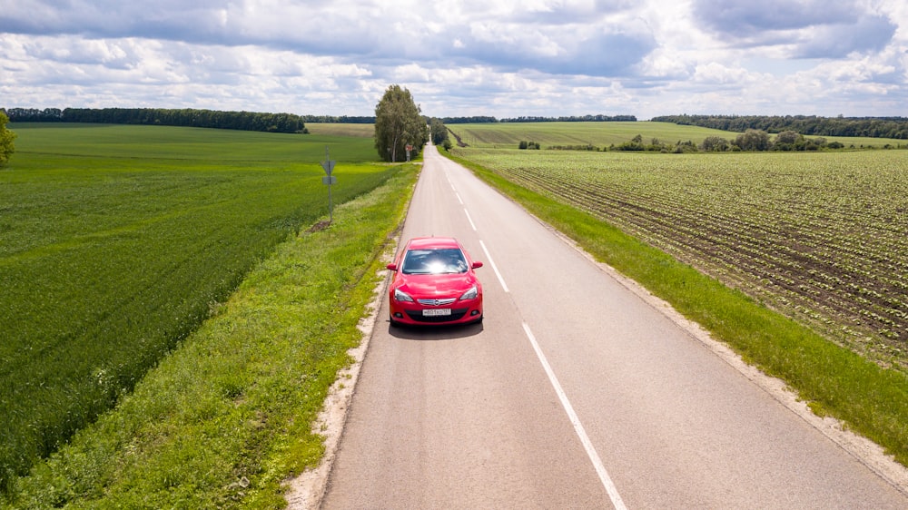 red car on road between green grass field during daytime