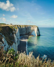 brown and green cliff beside blue sea under blue sky during daytime