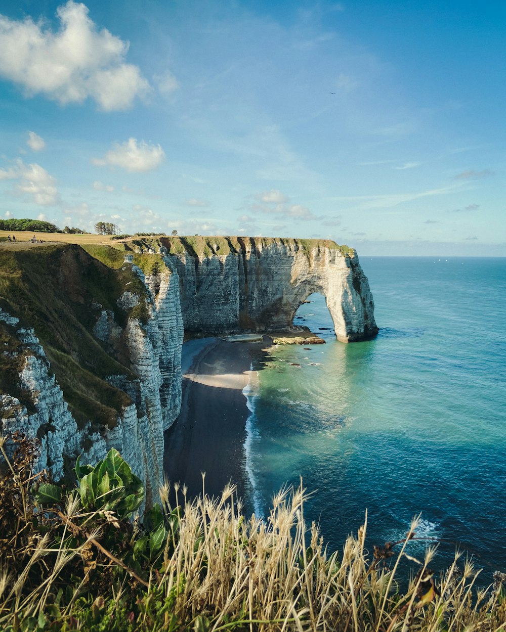 brown and green cliff beside blue sea under blue sky during daytime