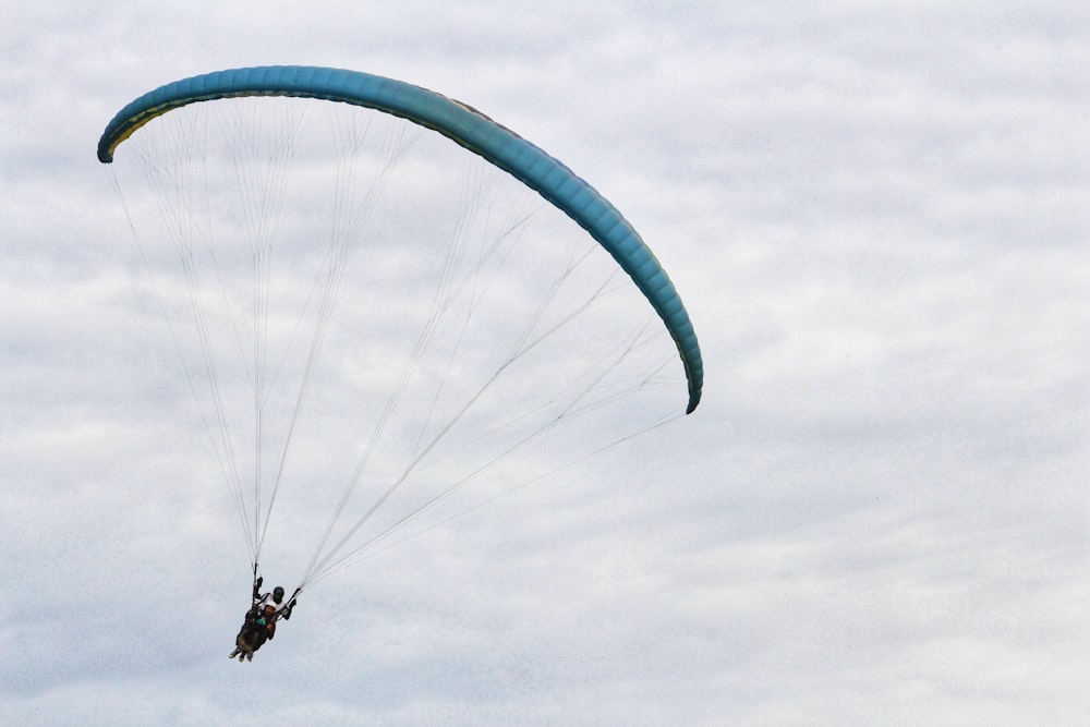 person riding on green parachute under white clouds during daytime