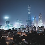 A city skyline at night with modern skyscrapers illuminated by artificial lights. The tall buildings create a striking urban landscape against the dark sky.