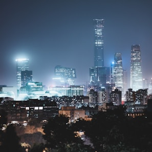 A city skyline at night with modern skyscrapers illuminated by artificial lights. The tall buildings create a striking urban landscape against the dark sky.