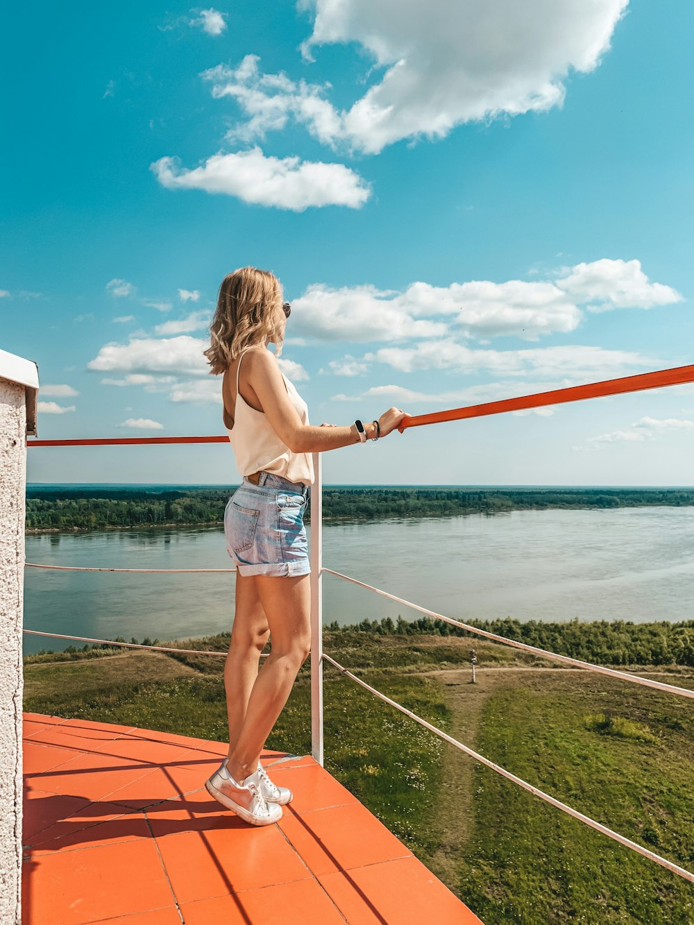 woman in pink shirt and blue denim shorts standing on red and white wooden dock during