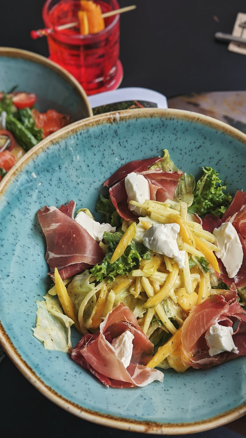 pasta with sliced tomato and green leaf vegetable on blue and white ceramic bowl