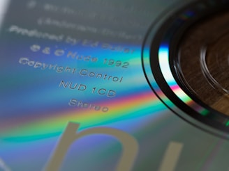 Close-up view of a compact disc with visible rainbow-like reflections and text printed on its surface. The text includes details such as 'Produced by Ed Buller', 'Nude 1992', 'Copyright Control', and 'Stereo'. The disc itself has a shiny, reflective surface with iridescent hues visible around the edges.