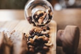 A glass jar is tipped over on its side, spilling out a mix of nuts and dried fruits onto a wooden cutting board. The assortment includes cashews, almonds, raisins, and hazelnuts, adding a rustic and natural vibe to the scene.