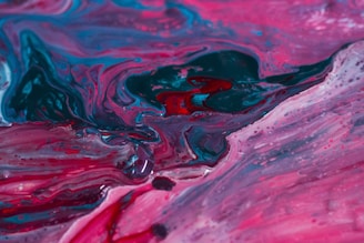 Colorful abstract painting with swirling patterns of red, pink, blue, and green. The paint appears to blend and flow, creating a sense of movement and fluidity.