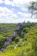 A picturesque medieval village nestled among lush green hills, with a historic church or castle perched on a rocky cliff. The sky is partly cloudy, allowing sunlight to illuminate the vibrant landscape. The architecture of the buildings is traditional, with red and brown rooftops.