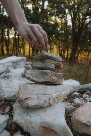Close-up of hands shaping natural stone for a garden pathway under soft daylight.