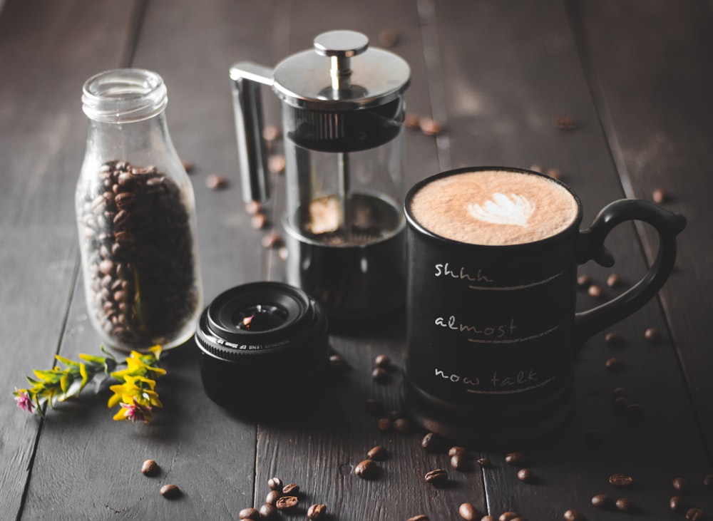 coffee in black ceramic mug beside coffee beans on black ceramic saucer