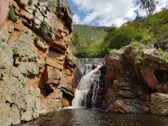 waterfalls between brown rocky mountain under white cloudy sky during daytime