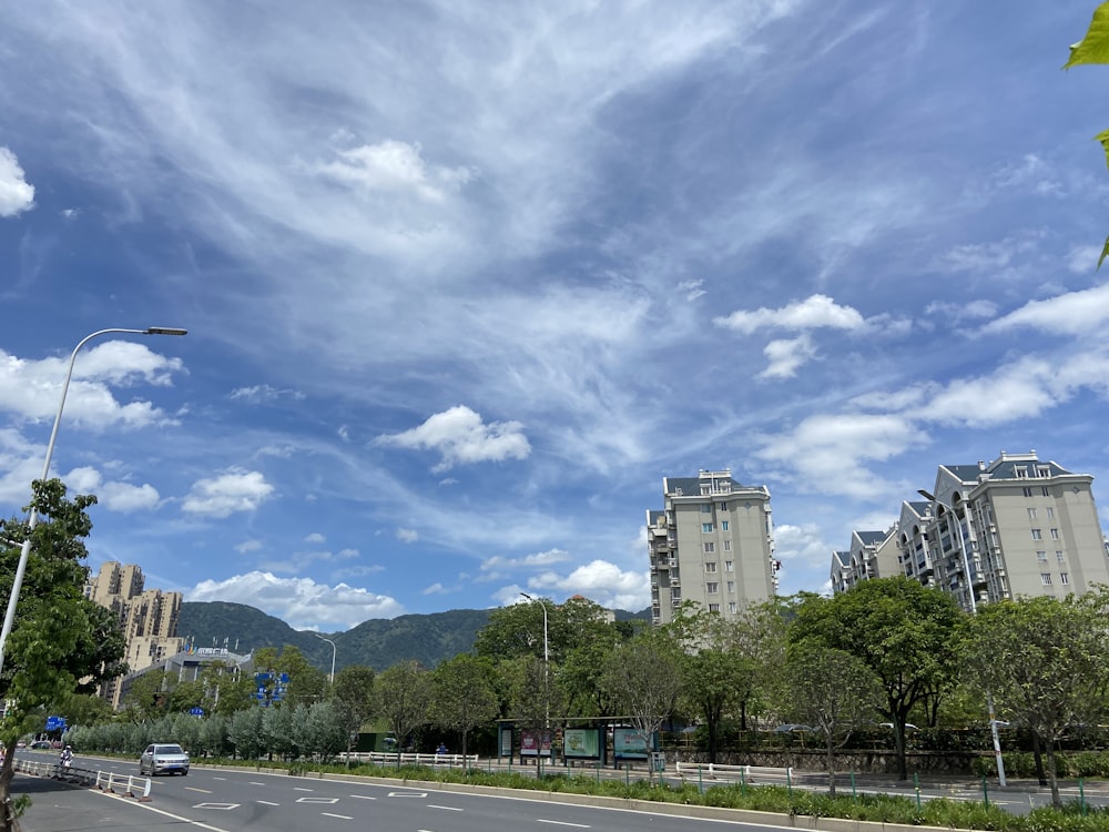 cars on road near trees and buildings under white clouds and blue sky during daytime