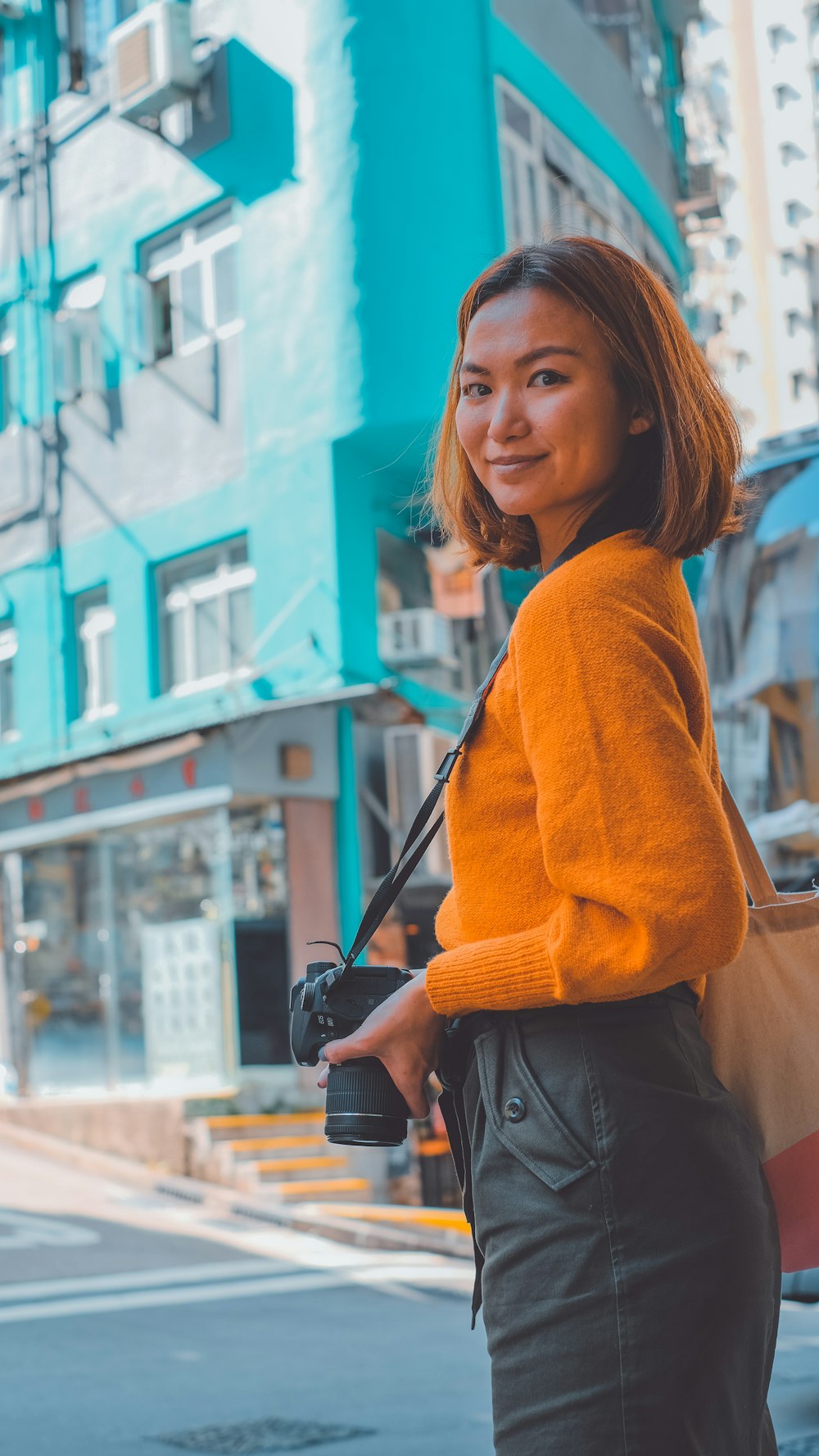 woman in orange sweater holding black dslr camera