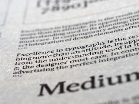 Close-up view of printed text on a textured paper surface. The focus is on the sentence 'Excellence in typography is the result of nothing more than an attitude.' The typeface and layout suggest a refined attention to typographic detail.