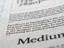 Close-up view of printed text on a textured paper surface. The focus is on the sentence 'Excellence in typography is the result of nothing more than an attitude.' The typeface and layout suggest a refined attention to typographic detail.
