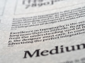Close-up view of printed text on a textured paper surface. The focus is on the sentence 'Excellence in typography is the result of nothing more than an attitude.' The typeface and layout suggest a refined attention to typographic detail.