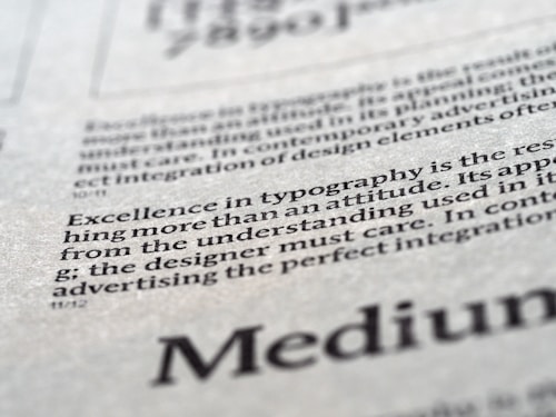 Close-up view of printed text on a textured paper surface. The focus is on the sentence 'Excellence in typography is the result of nothing more than an attitude.' The typeface and layout suggest a refined attention to typographic detail.