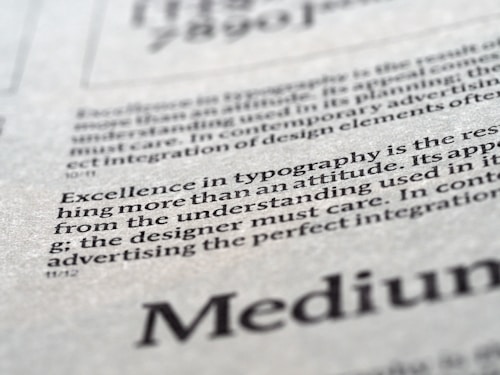 Close-up view of printed text on a textured paper surface. The focus is on the sentence 'Excellence in typography is the result of nothing more than an attitude.' The typeface and layout suggest a refined attention to typographic detail.