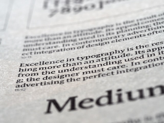Close-up view of printed text on a textured paper surface. The focus is on the sentence 'Excellence in typography is the result of nothing more than an attitude.' The typeface and layout suggest a refined attention to typographic detail.