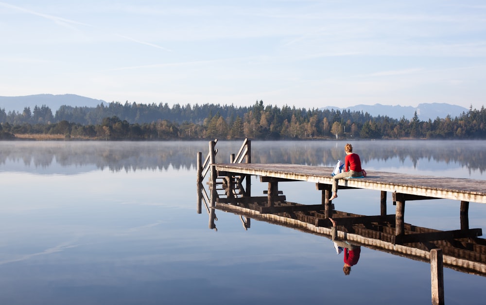 man and woman sitting on wooden dock over the lake during daytime