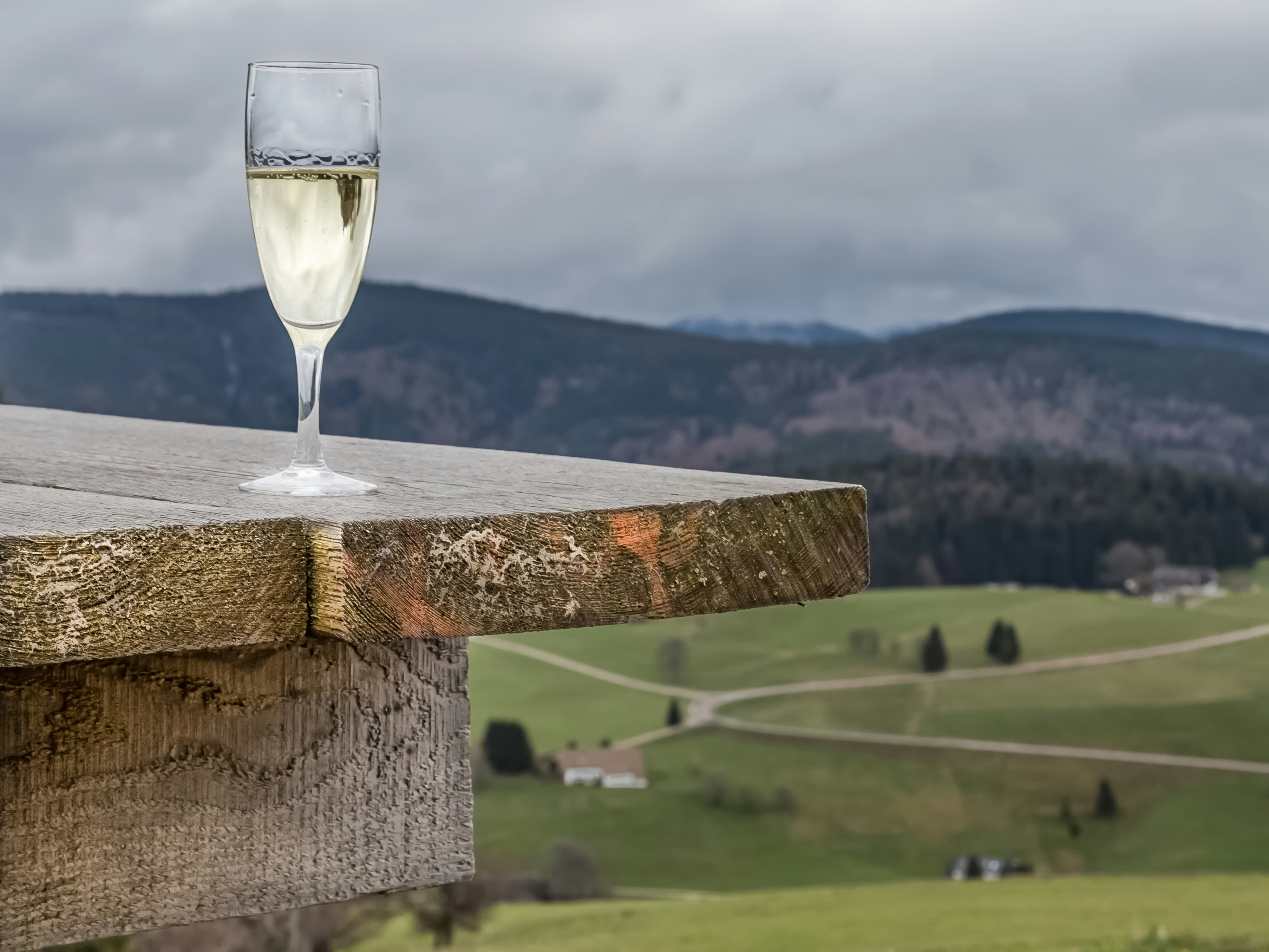 Glass of sparkling wine on a stand over green hills