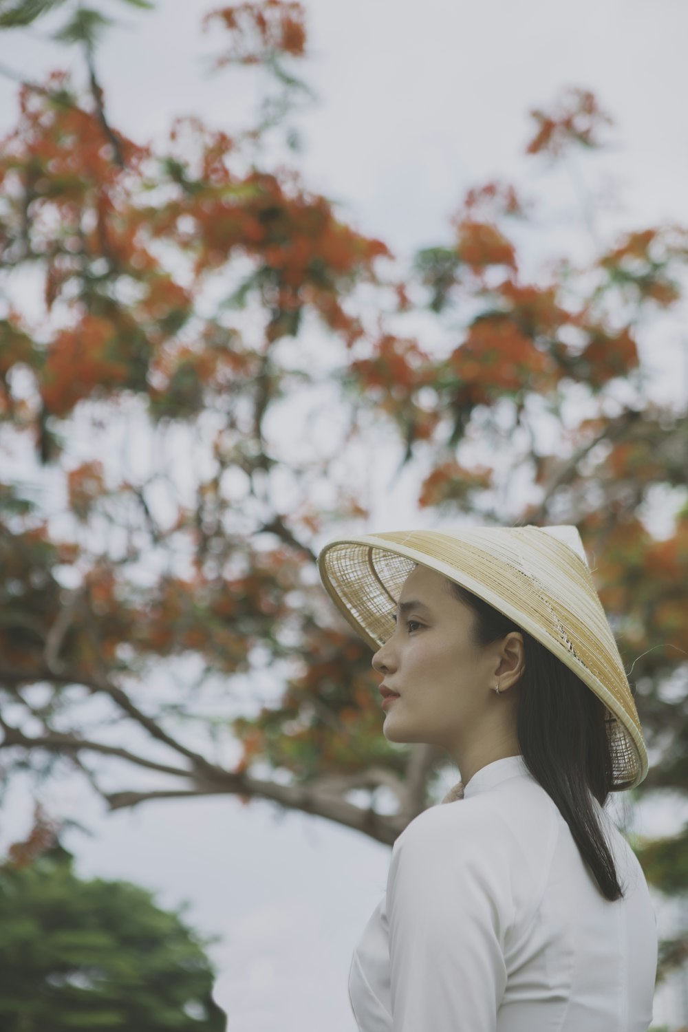 woman in white sun hat and white shirt standing near red flowers