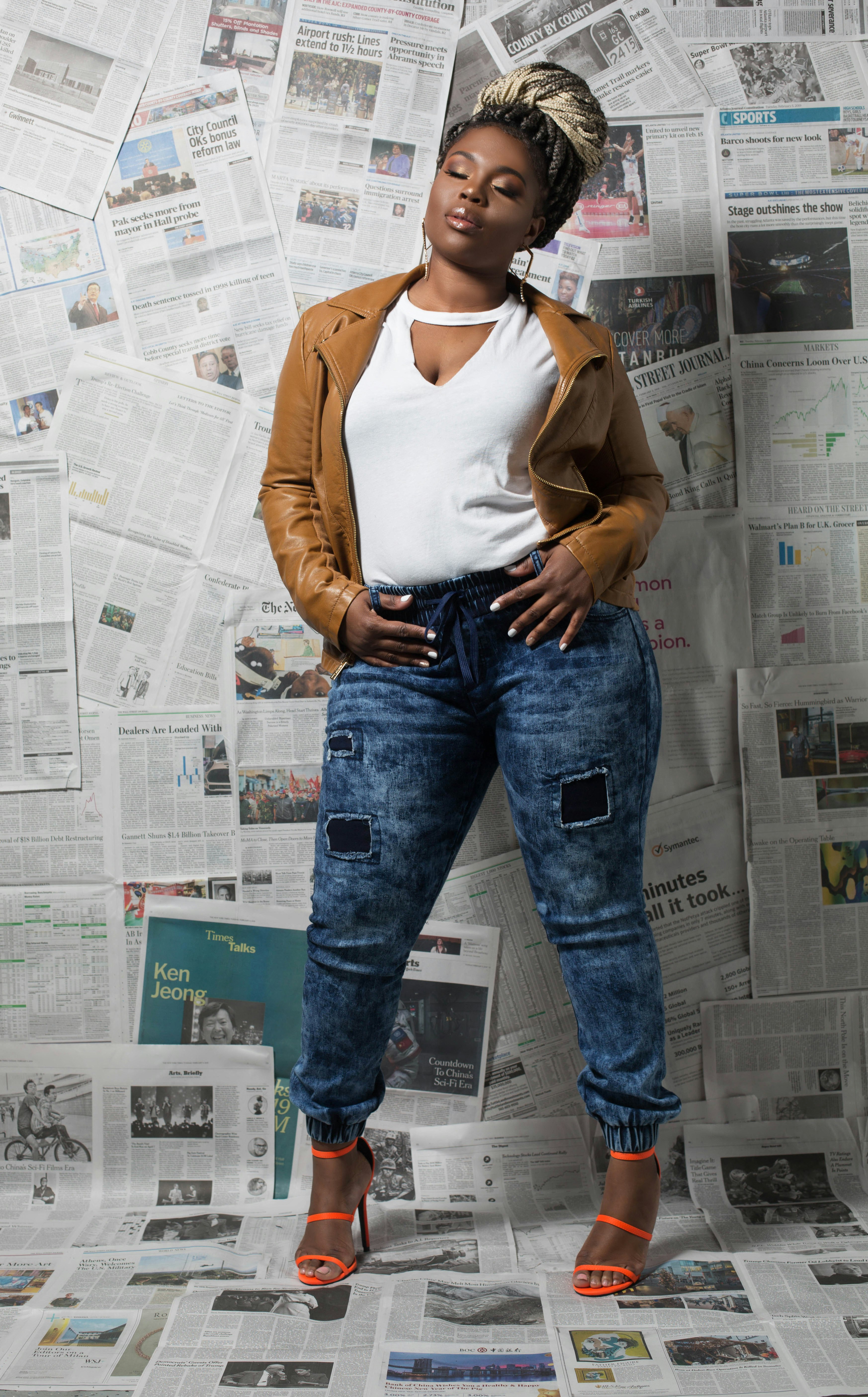 woman in brown cardigan and blue denim jeans standing beside white wall