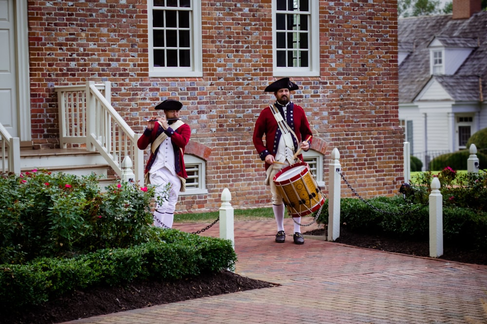 2 men playing musical instruments near brown brick building during daytime