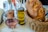 A wicker basket contains a loaf of rustic bread alongside a glass of rosé wine, and two glass bottles filled with oil and vinegar. The setting is on a table covered with a white tablecloth, and cutlery is partially visible next to the basket.