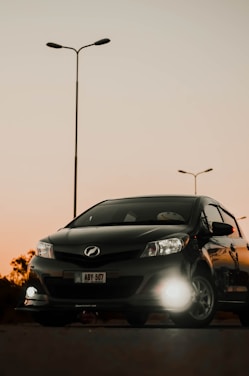 A sleek black luxury sedan parked in front of a vibrant Charlotte city skyline at sunset.