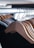 A row of natural wood hangers is aligned neatly on a metal rack, casting shadows and showing the smooth texture of the wood. The hangers hold dark-colored garments in a softly lit environment, suggesting a clothing store or wardrobe setting.