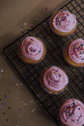 A smiling baker holding a tray of freshly baked cupcakes with pink and white icing.