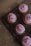 Five cupcakes with pink frosting and colorful sprinkles are arranged on a black cooling rack. The cupcakes are placed on a brown paper background with scattered sprinkles around the rack.