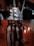A decadent milkshake topped with whipped cream and chocolate sauce, served in a large glass jar. An Oreo cookie is placed on the side, and two straws extend from the top. The background has a warm, dimly lit ambiance, suggesting a cozy setting.
