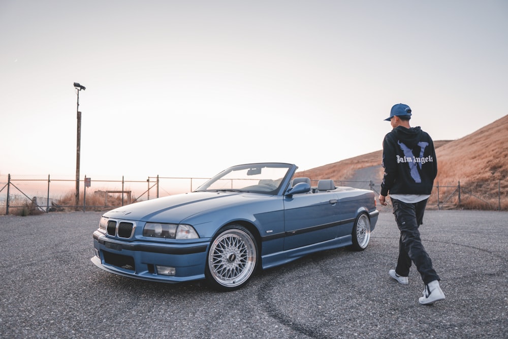 man in black jacket standing beside blue car during daytime