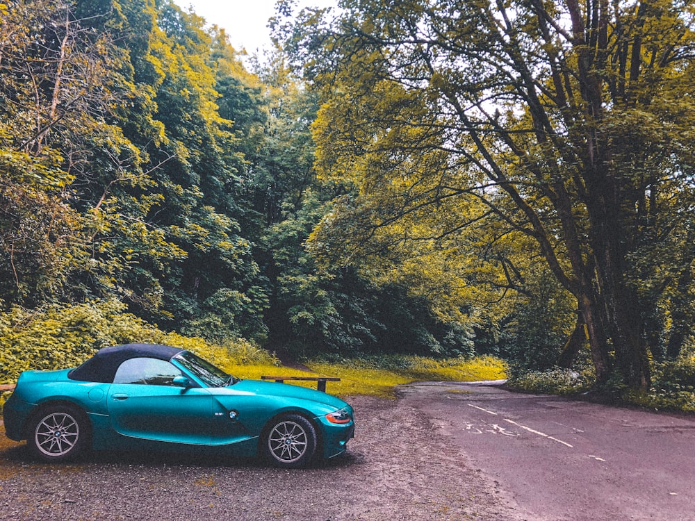 blue coupe on road between green trees during daytime