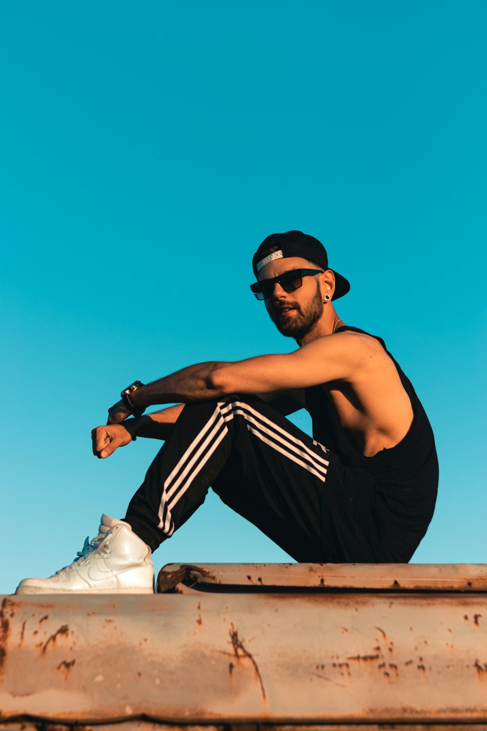 man in black tank top wearing black sunglasses and black cap sitting on brown wooden bench