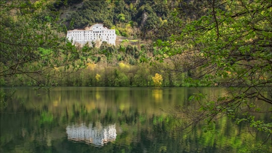 white concrete building near green trees and body of water during daytime in Monticchio Italy