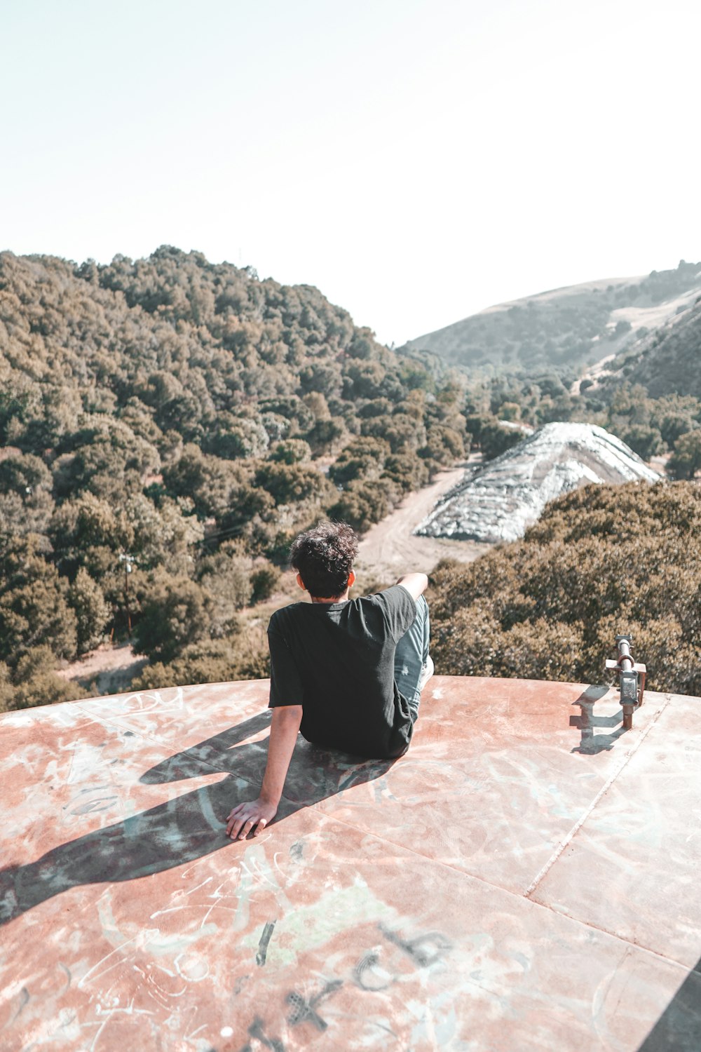 man in black t-shirt and gray shorts sitting on concrete wall during daytime