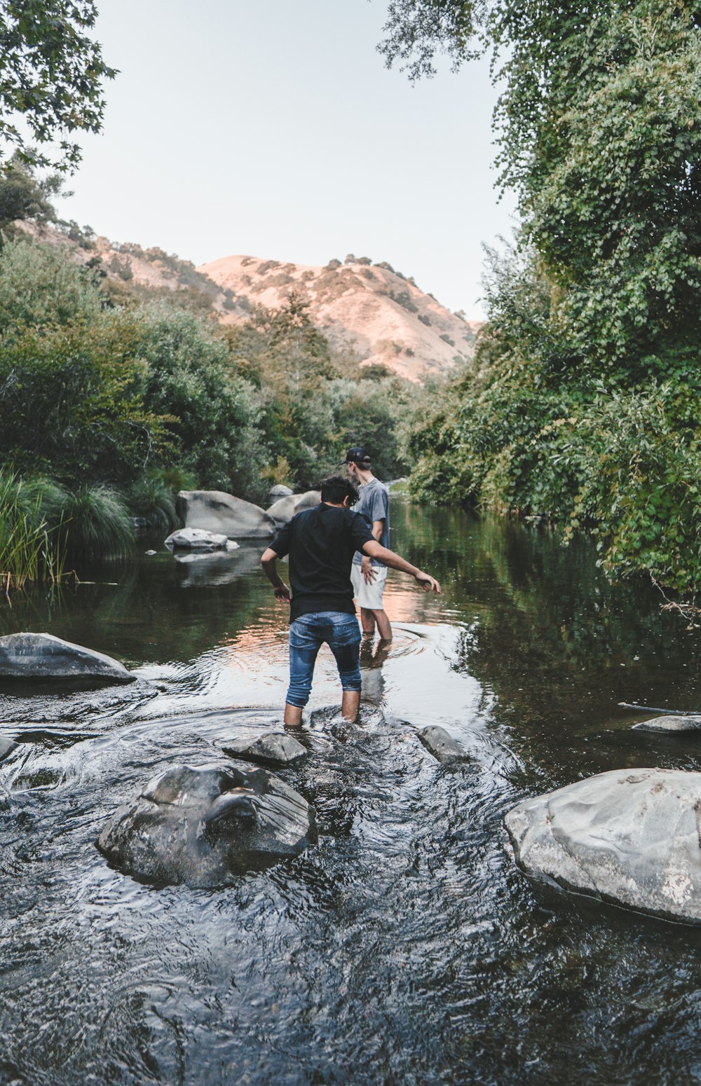 man in blue shirt and black pants sitting on rock in river during daytime