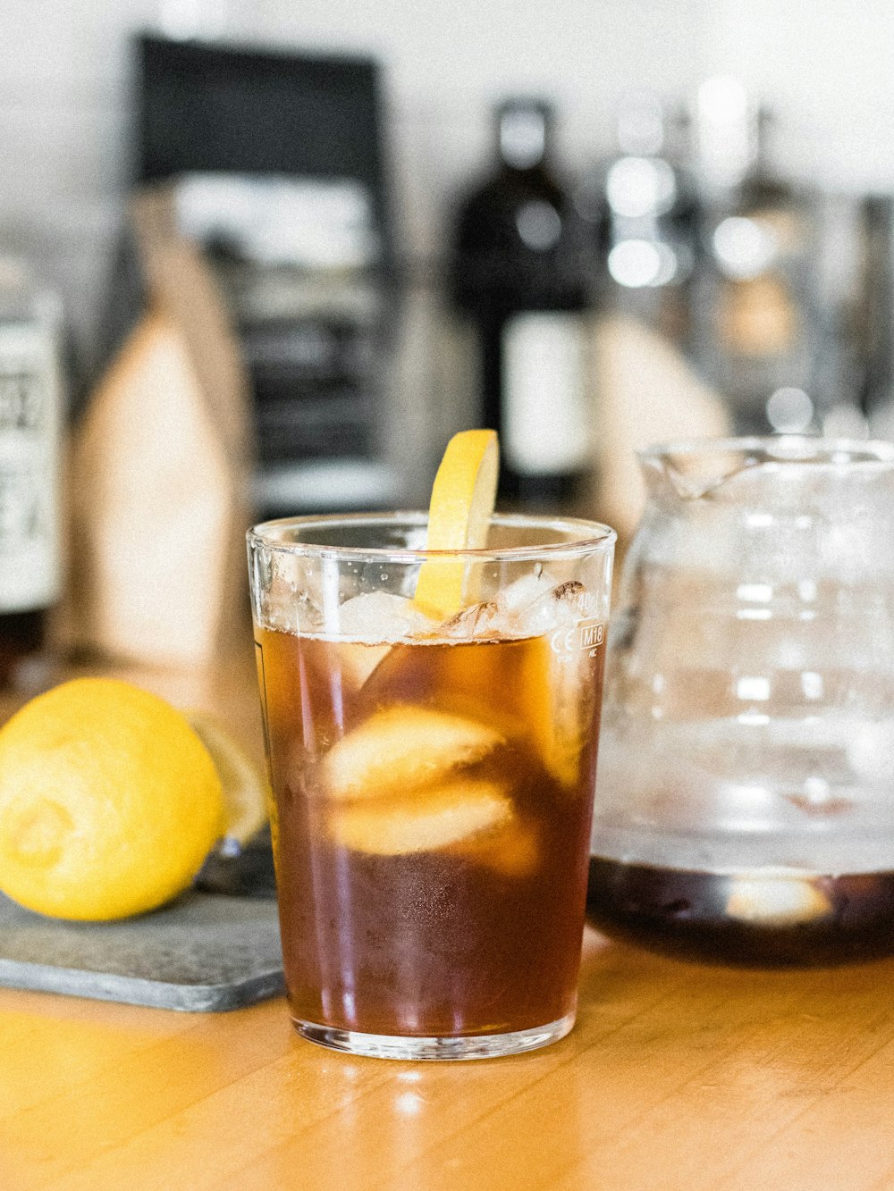 clear drinking glass with brown liquid and lemon on brown wooden table