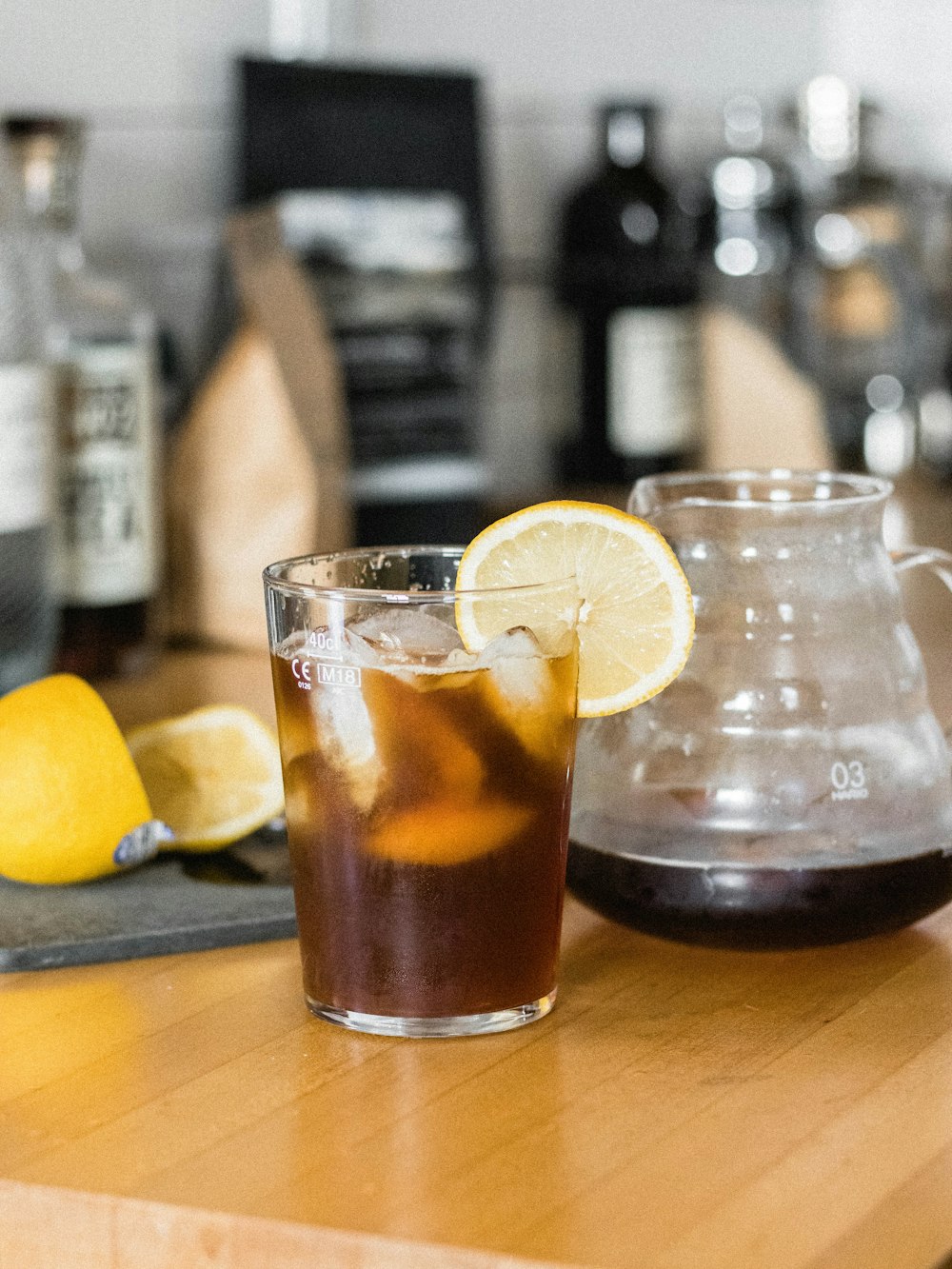 clear drinking glass with brown liquid and lemon on brown wooden table