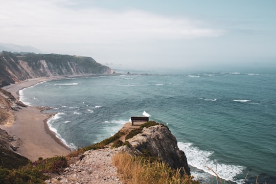 white and black lighthouse on brown and green cliff by the sea during daytime in Asturias Spain