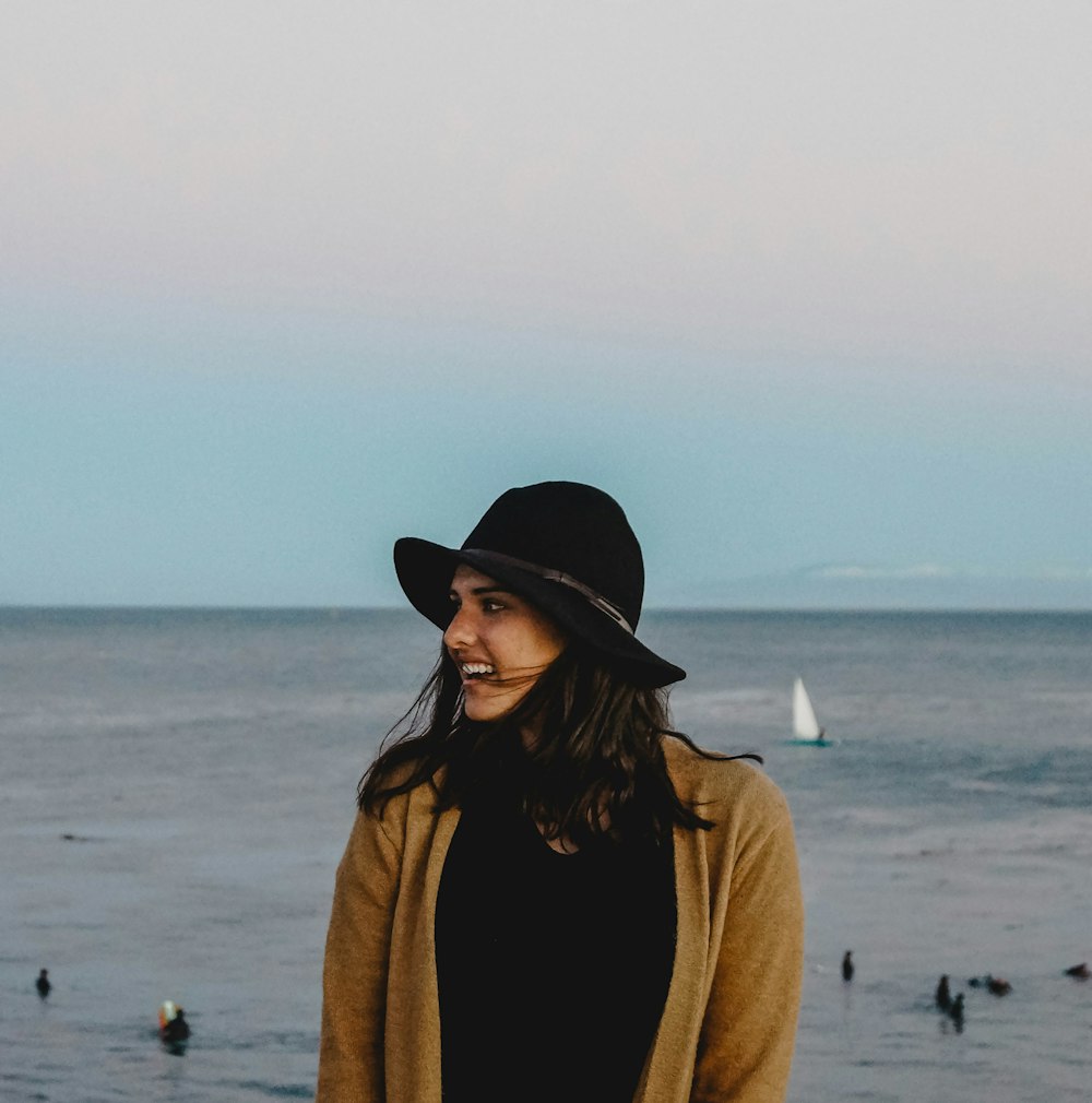 woman in brown coat and black fedora hat standing on beach during daytime
