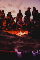 people sitting on brown sand near bonfire during night time