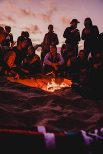 A group of diverse people gathered outdoors, engaging in deep conversation around a campfire at sunset.