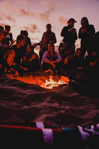 people sitting on brown sand near bonfire during night time