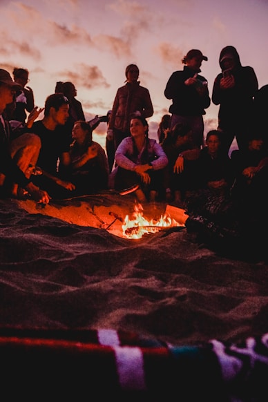 A group of diverse travelers sharing stories around a campfire at dusk.