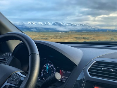 A close-up of a car dashboard driving through winding Swiss Alps roads under cloudy skies.