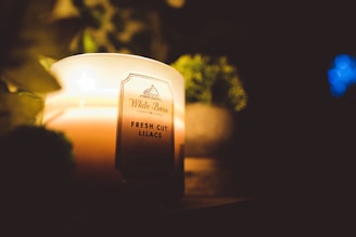 A calming lavender candle casting a gentle light in a serene bedroom setting.